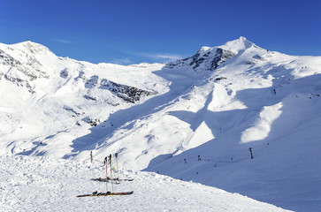 Two pairs of skis, ski poles, ski lifts and pistes and Hintertux Glacier in Zillertal Alps in Austria at sunset light