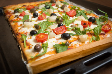 Pizza vegetariana con mozzarella, sugo, pomodorini, rucola, cipolle, olive, capperi e origano