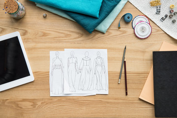 top view of seamstress workplace on table with fabric, tablet and sketches