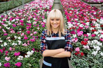 Beautiful young woman flower center worker , standing with crossed hands looking at camera and smiling. Work in greenhouse