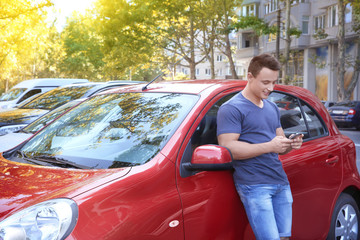 Young man with mobile phone near car outdoors
