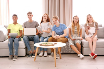 Group of teenagers with modern gadgets and tasty pizza at home