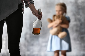 Woman with bottle of alcohol and blurred girl on grey background - obrazy, fototapety, plakaty