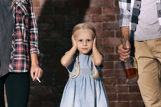 Parents with bottle of alcohol and little girl against brick background