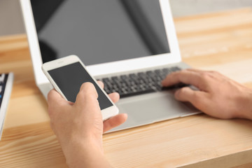 Man using cell phone and laptop on table, closeup