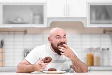 Overweight young man with unhealthy food at table in kitchen