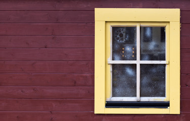 Fototapeta na wymiar Christmas fair cabin's window with snow pattern on brown wooden wall with copy space. Light yellow window with brown plank background