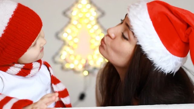 Portrait of a happy mother and her child in Santa Claus costumes for Christmas. Mom embraces with love the daughter and kisses. New year and magic. Close-up