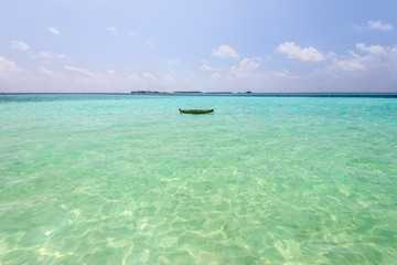 Empty tropical beach background. Horizon with resort island, sky and a small wooden boat in Maldives.