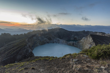 Fog drifts past Danau Kootainuamuri crater as the sun rises in the distance at Kelimutu National Park in Indonesia.