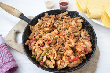 Chicken stew with red and green pepper, with red onion, pickled cucumber and spices in a frying pan.