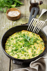 Fritatta with potatoes, green peas and herbs in an iron frying pan on an old wooden background. Selective focus. Rustic style.