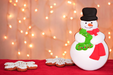 Christmas gingerbread snowman and snowflakes on a red velvet with light garlands. Concept of new year gift. Picture for a confectionery catalog. Invitation or greeting card with copy space.