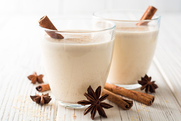Homemade eggnog with grated nutmeg and cinnamon on white wooden table. Traditional Christmas drink.