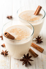 Homemade eggnog with grated nutmeg and cinnamon on white wooden table. Traditional Christmas drink.