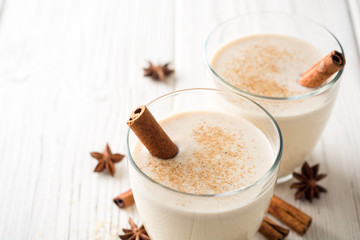 Homemade eggnog with grated nutmeg and cinnamon on white wooden table. Traditional Christmas drink.