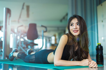 Fototapeta na wymiar Sports woman lying and relaxing on yoga mat in fitness gym with sports equipment background. Beauty and Workout training exercise concept. Body build up and Strength theme.