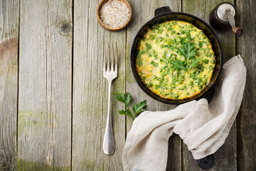 Fritatta with potatoes, green peas and herbs in an iron frying pan on an old wooden background....