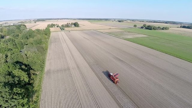 Aerial view of potato harvester on a beautiful landscape with blue skies