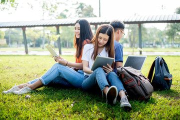Fototapeta na wymiar Group of Asian college student using tablet and laptop on grass field at outdoors. Technology and Education learning concept. Future Technology and Modern entertainment concept. Edutainment theme.