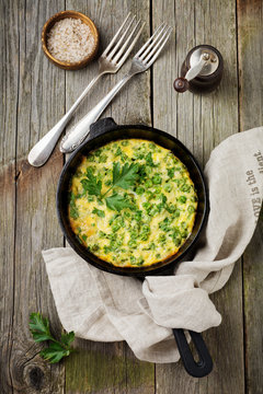 Fritatta with potatoes, green peas and herbs in an iron frying pan on an old wooden background. Selective focus. Rustic style.Top view.