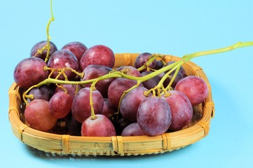 Bunch of black grapes in wicker basket over blue background