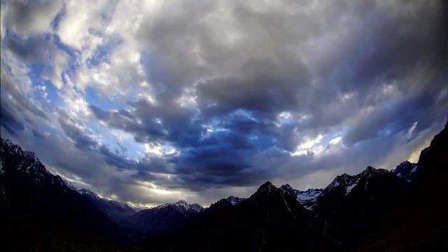 Swirling dark clouds in the blue sky over the high snowy mountains in Karakorum Pakistan