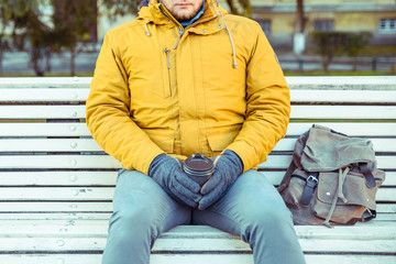 man waiting on the bench of city park with cup of coffe