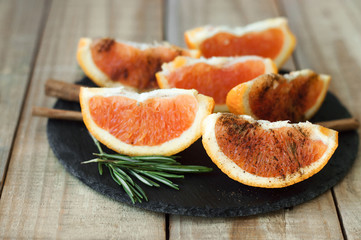 Naklejka na ściany i meble Orange with cinnamon powder and rosemary served on black slate board on wooden table. Portion of sliced orange fruit. Healthy dessert
