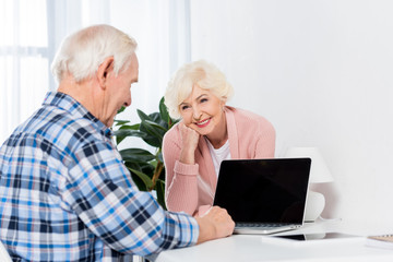 portrait of senior woman looking at husband using laptop with blank screen at home