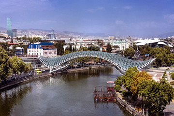 Fototapeta na wymiar Kingdom of Georgia, Tbilisi (Tiflis): Panoramic view with Bridge of Peace over Kura river with, Serice Hall, National Bank, skyscrapers and skyline of the Georgian capital in the background. 