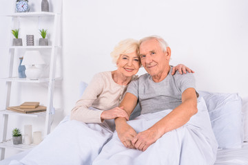 Fototapeta na wymiar portrait of smiling senior couple resting in bed and looking at camera at home