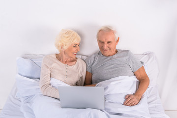 senior couple using laptop while resting in bed at home
