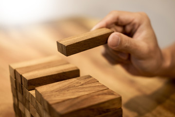 Hand of engineer playing a blocks wood tower game on blueprint or architectural project concept.