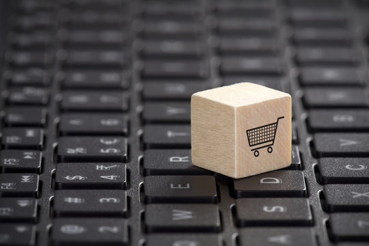 Wooden block with shopping cart graphic on laptop keyboard. Online shopping concept. 