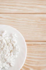Close-up white plate with fresh curd on wooden table with copy space. Top view.