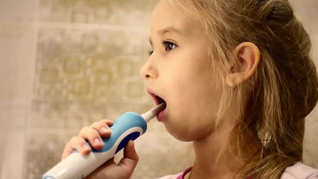 Beautiful young girl brushes teeth by electric brush, smiling, drops out milk teeth, concept of health.