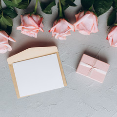 Blank paper note with envelope, gifts and pink rose on a gray background.
