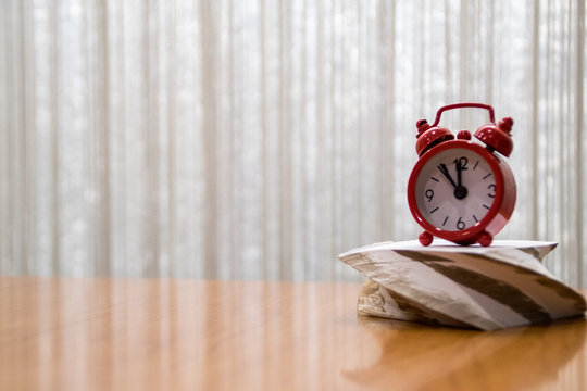 on the right side of the empty table red clock  standing on a block of paper,, Paper work against time