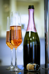 A festive morning for a couple. Two filled glasses and a bottle of rose sparkling wine. A bottle cork in a close up. Light blurred background.