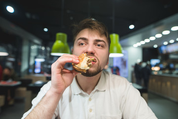 A hungry man enjoys a delicious burger at a fast food restaurant. The man eats fast food.