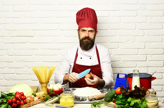 Man with beard breaks egg with knife on white background