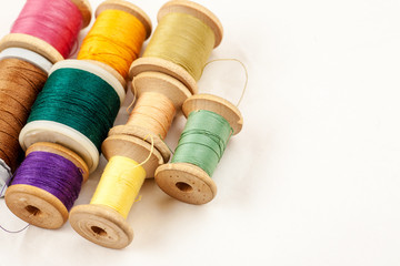 Different colour thread on wooden spools on a white background
