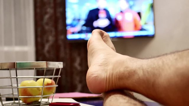 TV, television watching news with feet on the table and remote in hand.