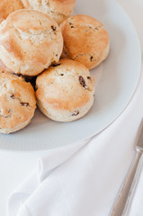 Freshly baked traditional British Buttermilk scones with raisins on white plate with cloth napkin and vintage knife on white kitchen table