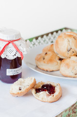 Freshly baked traditional British Buttermilk scones with raisins on white plate with cloth napkin and jar of homemade red currant jelly or jam on green vintage metal tray with rust on white table