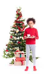 Portrait of cute mixed race little boy standing near Christmas tree with plate of cookies and glass of milk