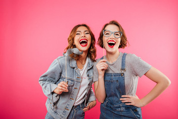 Funny women friends holding fake moustache and glasses.