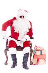 Portrait of swaggy Santa Claus in sunglasses relaxing in chair on white background