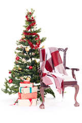 Empty chair with blanket on it near Christmas tree and stack of gift boxes on white background